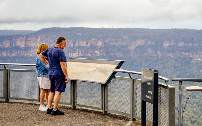 Tourists reading an information board overlooking the Blue Mountains, Australia.