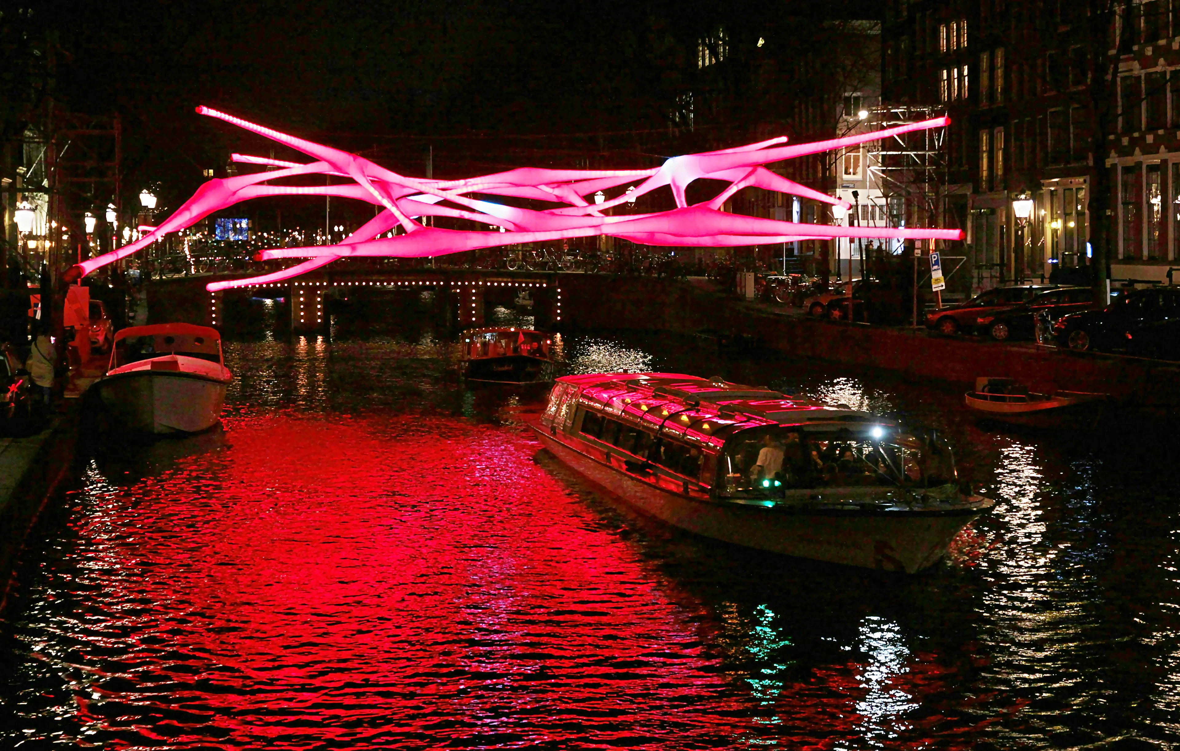 Canal cruise under illuminated art installation at Amsterdam Light Festival.