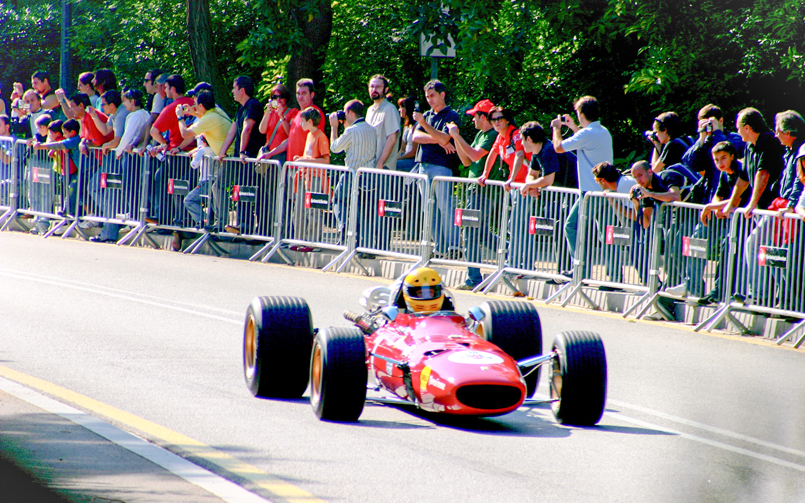 Race car on Montjuïc Park Circuit with spectators behind barriers.