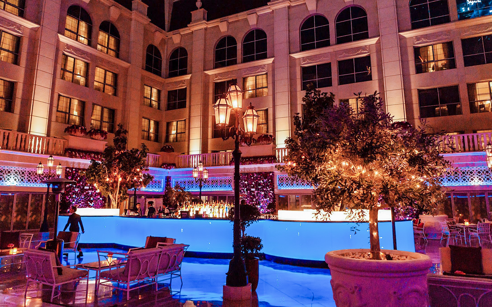 Outdoor dining area at Le Patio Restaurant, featuring illuminated trees and a bar, part of La Perle By Dragone experience.