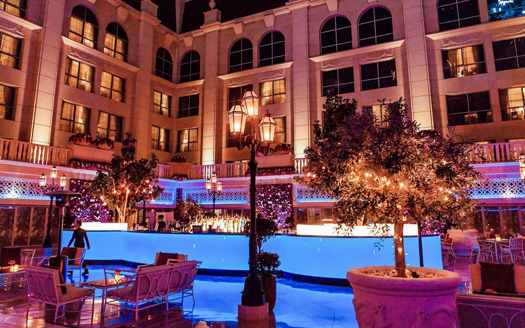 Outdoor dining area at Le Patio Restaurant, featuring illuminated trees and a bar, part of La Perle By Dragone experience.