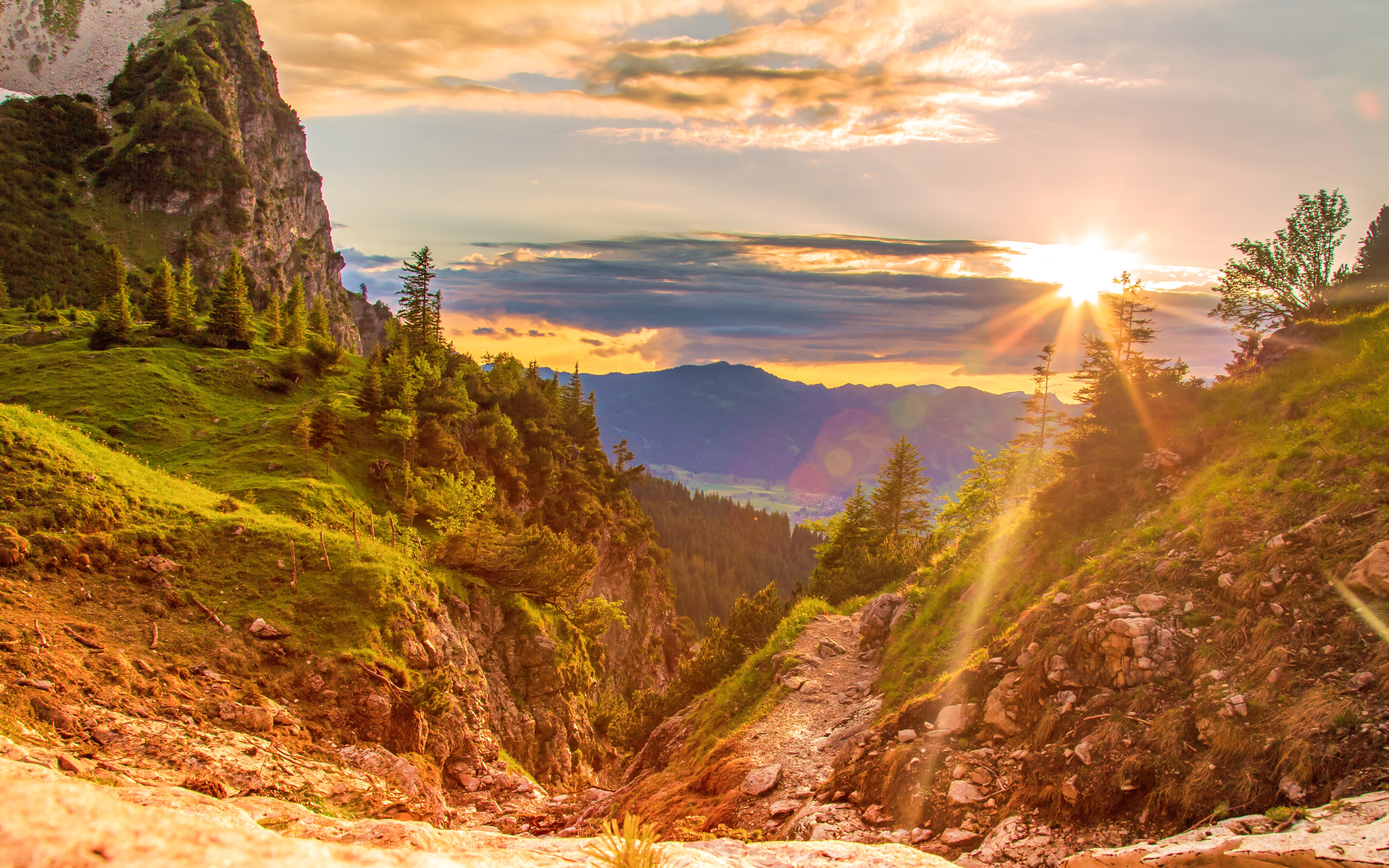 Alpsee sunset over lush green hills and rocky path in the Bavarian Alps.