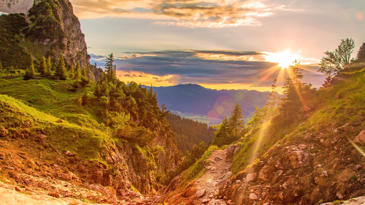 Alpsee sunset over lush green hills and rocky path in the Bavarian Alps.