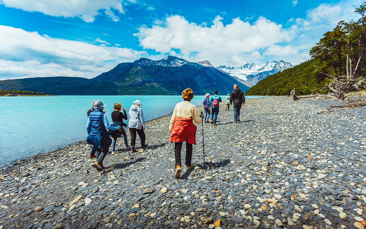 Hikers walking along the rocky shore of Argentino Lake in Los Glaciares National Park, Patagonia.