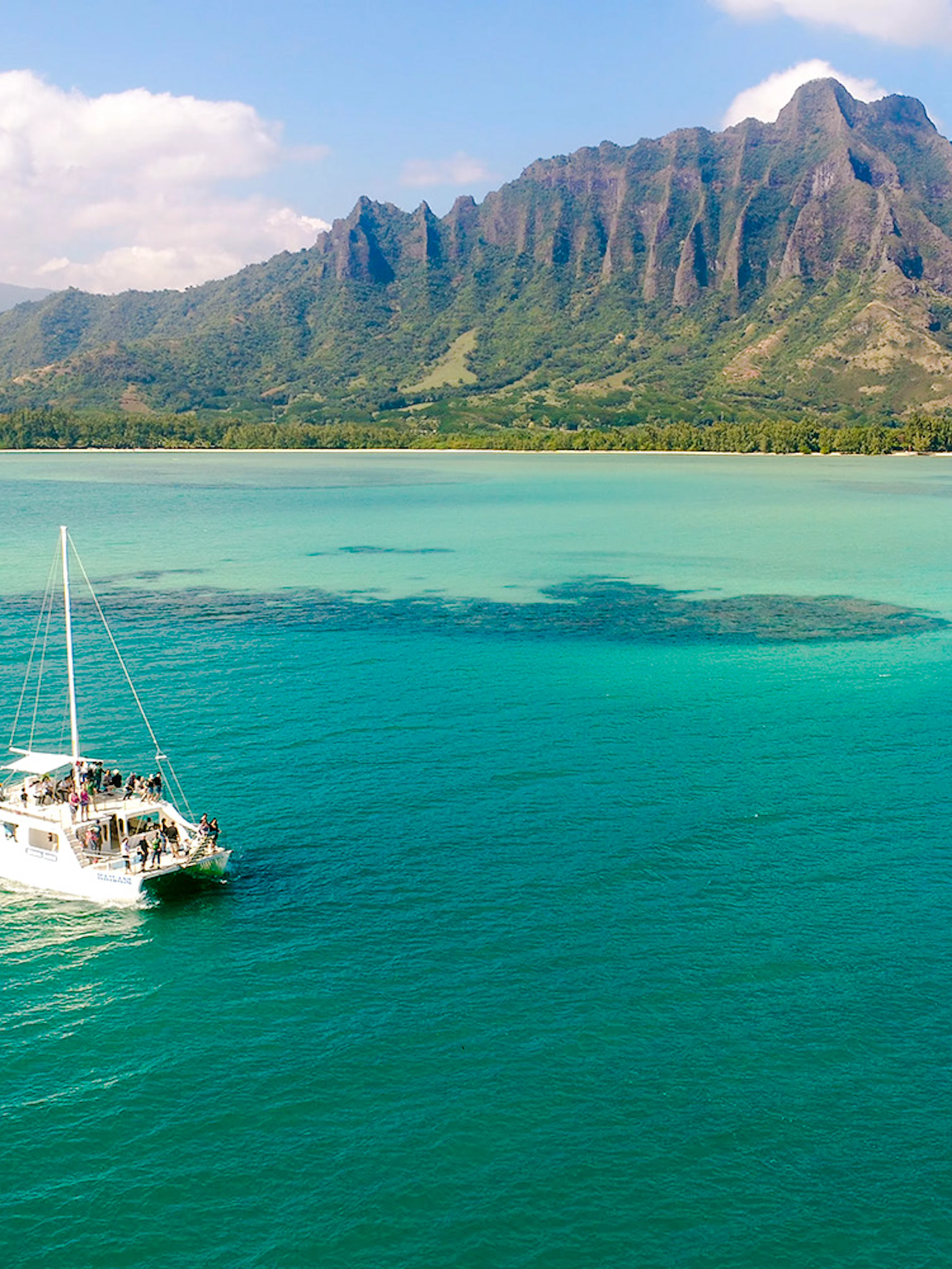 Catamaran sailing near Kualoa Ranch, Hawaii with lush mountains in the background.