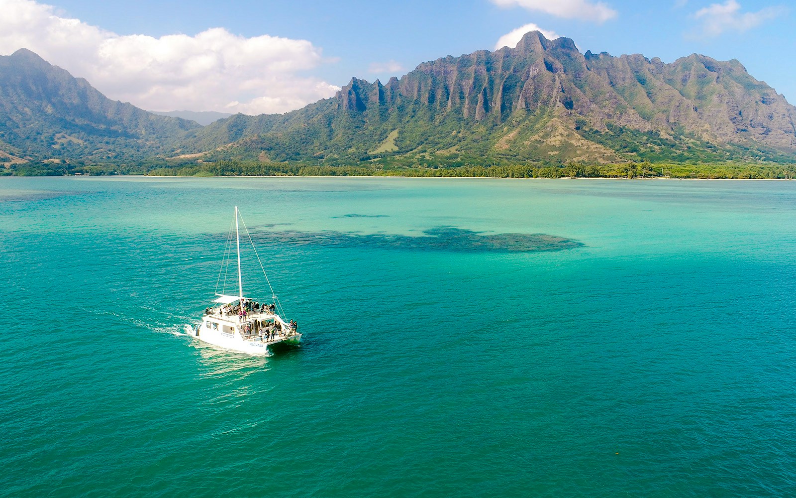 Catamaran sailing near Kualoa Ranch, Hawaii with lush mountains in the background.