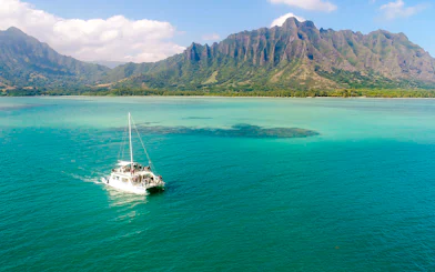 Catamaran sailing near Kualoa Ranch, Hawaii with lush mountains in the background.