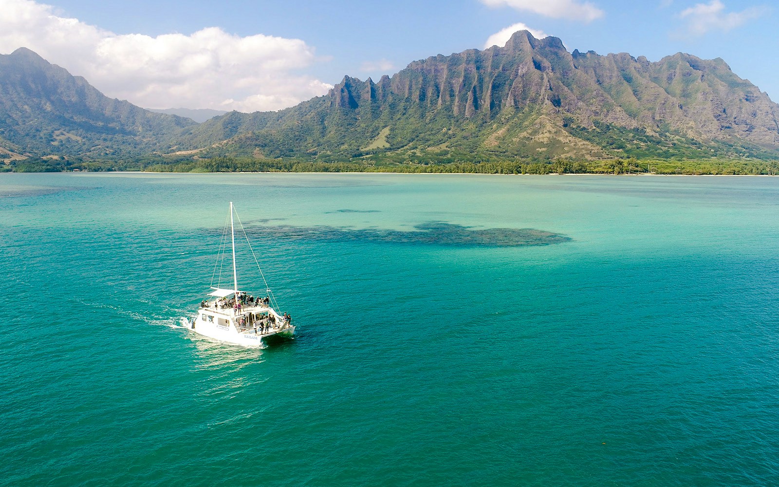 Catamaran sailing near Kualoa Ranch, Hawaii with lush mountains in the background.