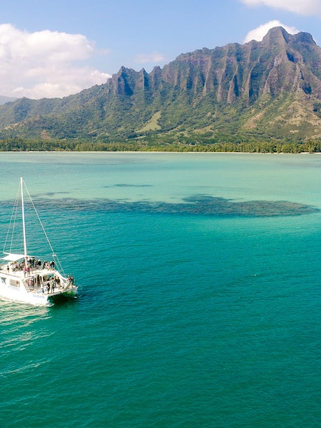 Catamaran sailing near Kualoa Ranch, Hawaii with lush mountains in the background.