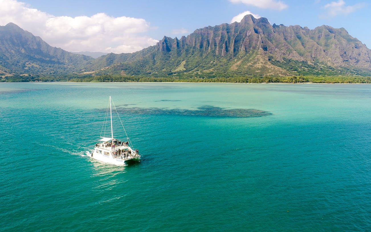 Catamaran sailing near Kualoa Ranch, Hawaii with lush mountains in the background.