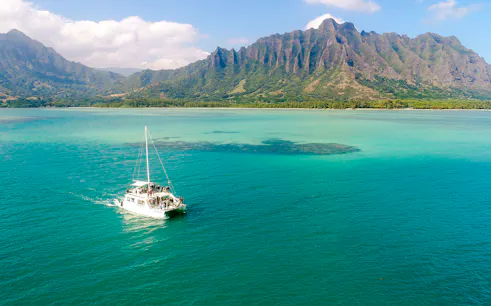 Catamaran sailing near Kualoa Ranch, Hawaii with lush mountains in the background.