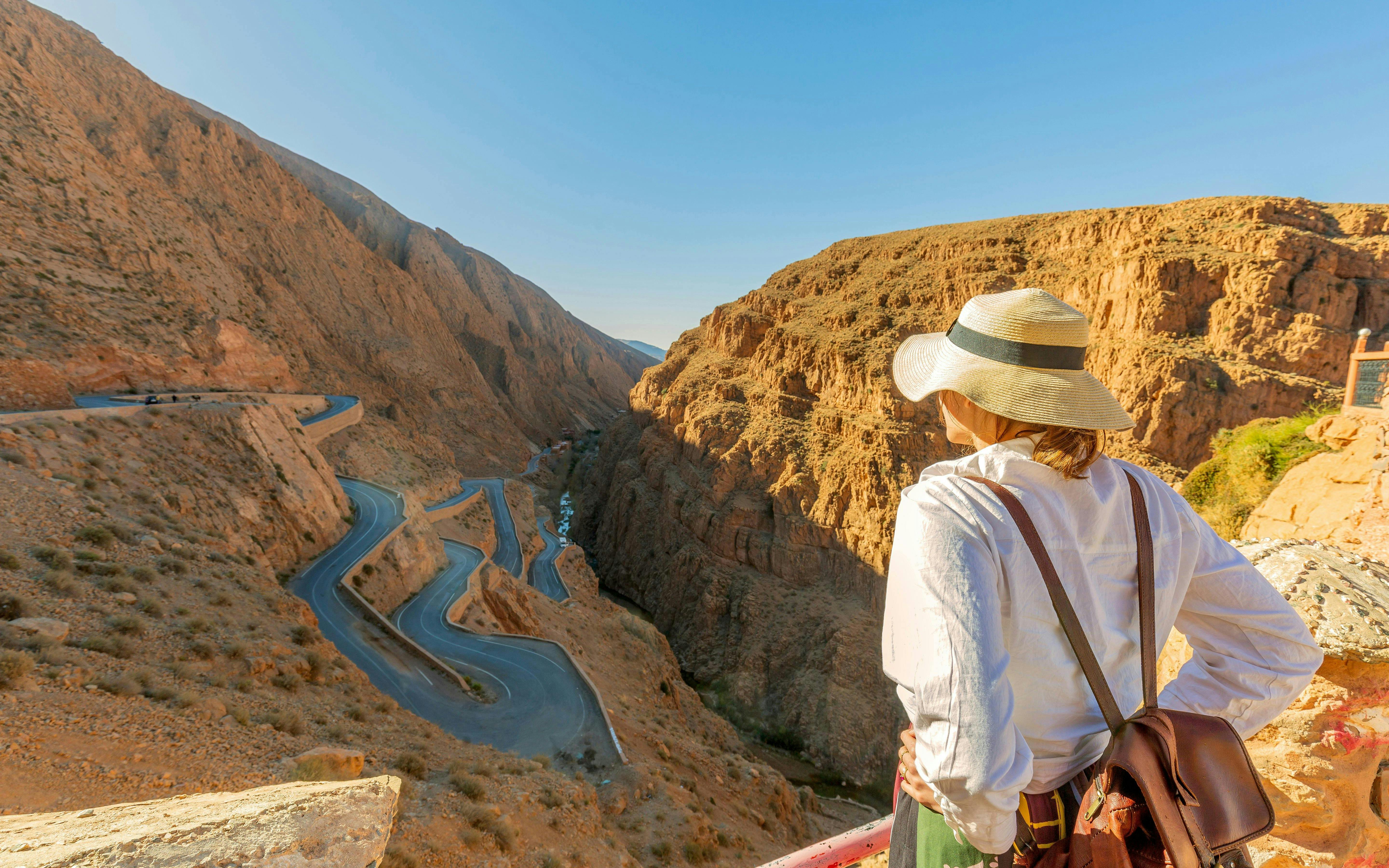Traveler overlooking winding road through Todra Gorge cliffs, Morocco.
