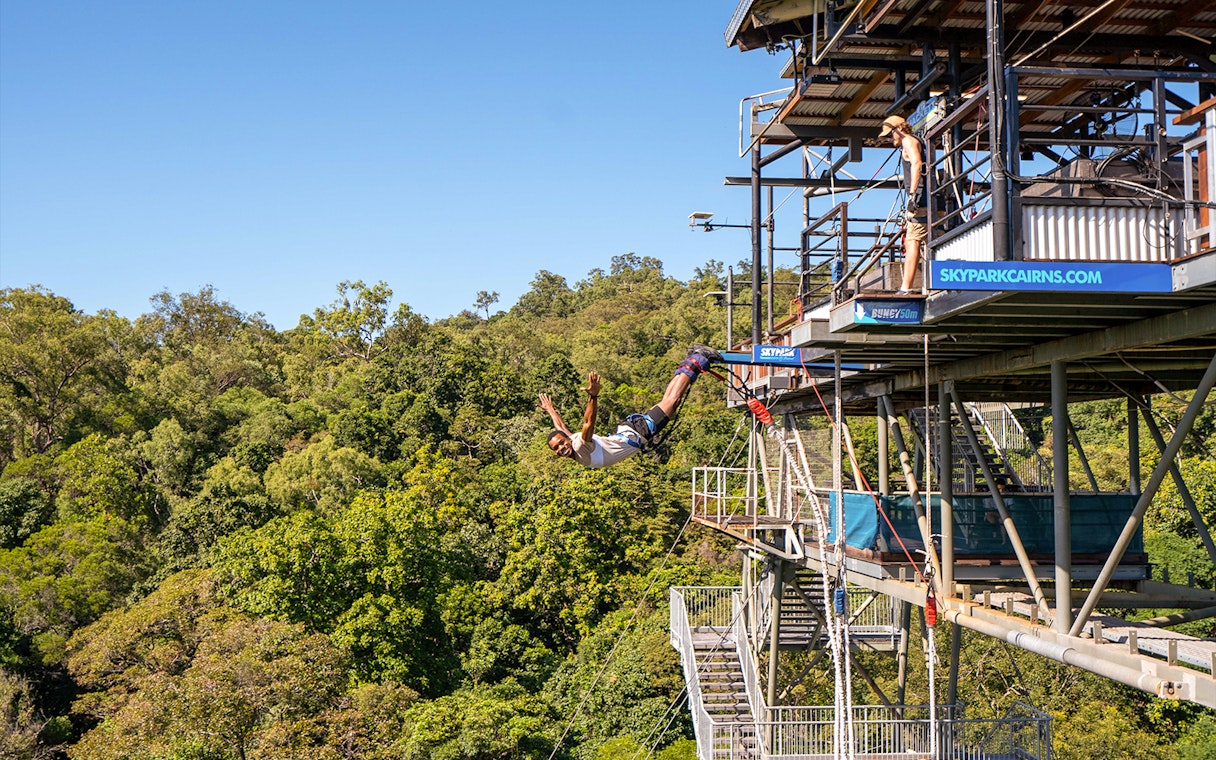 Person bungy jumping from platform at Skypark Cairns, surrounded by lush greenery.