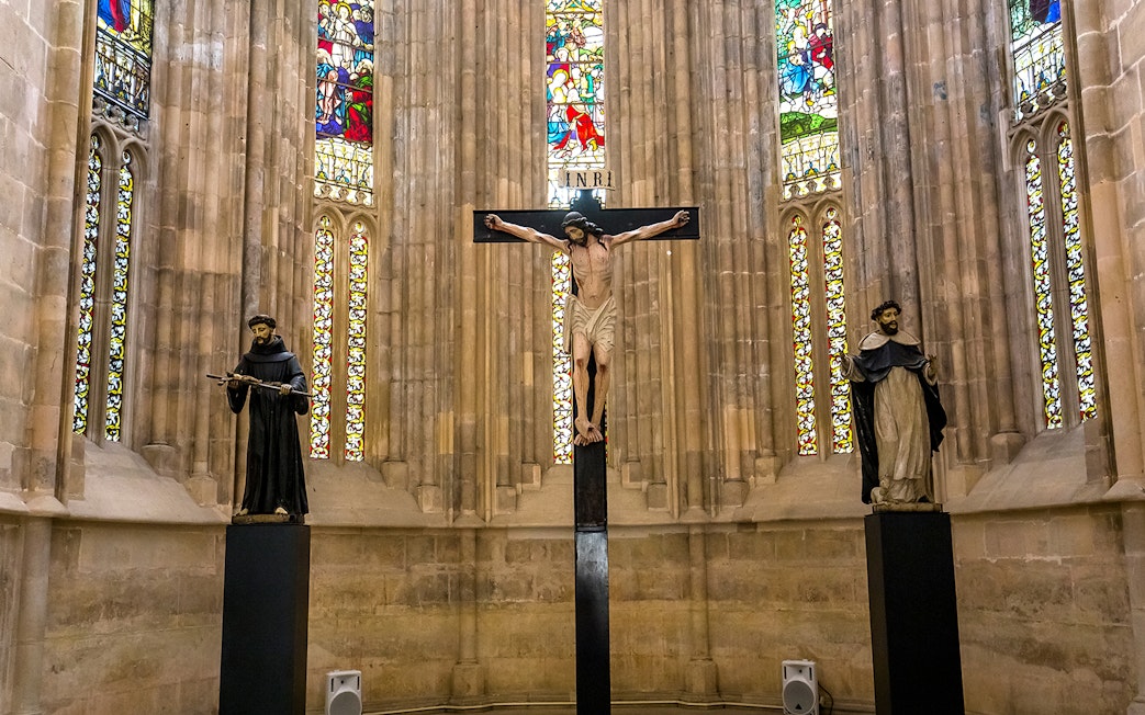 Crucifix and statues inside Batalha Monastery with stained glass windows.