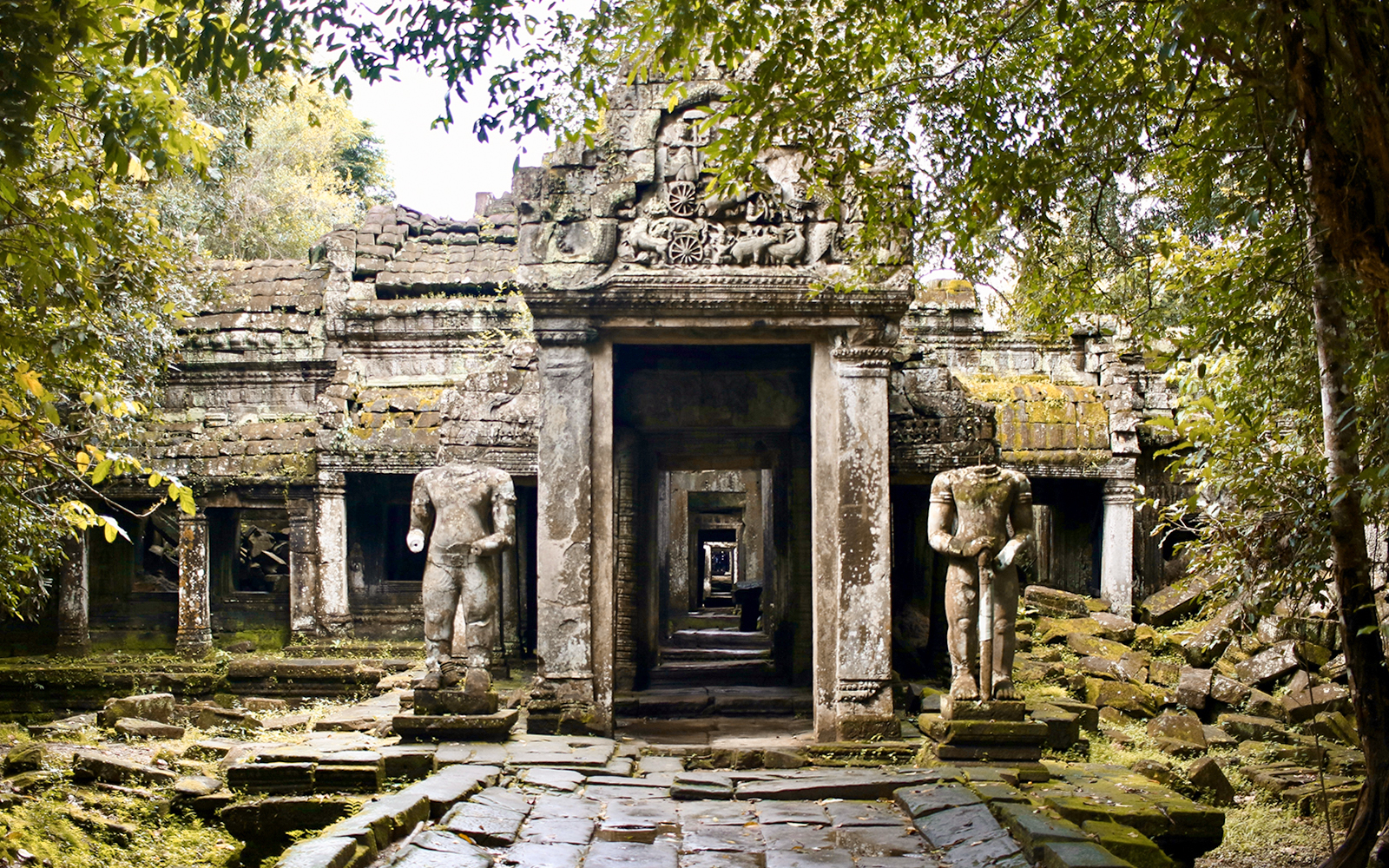 Ancient temple ruins with headless statues surrounded by lush greenery, resembling an Indiana Jones set.
