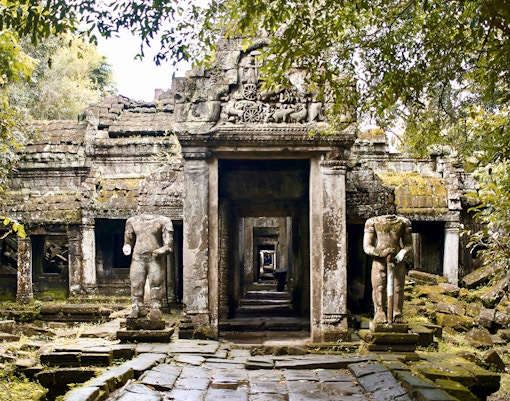 Ancient temple ruins with headless statues surrounded by lush greenery, resembling an Indiana Jones set.