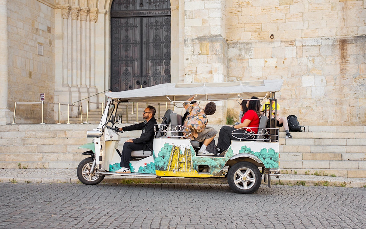 Tourists on an eco tuk tuk tour in Lisbon, passing a historic stone building.