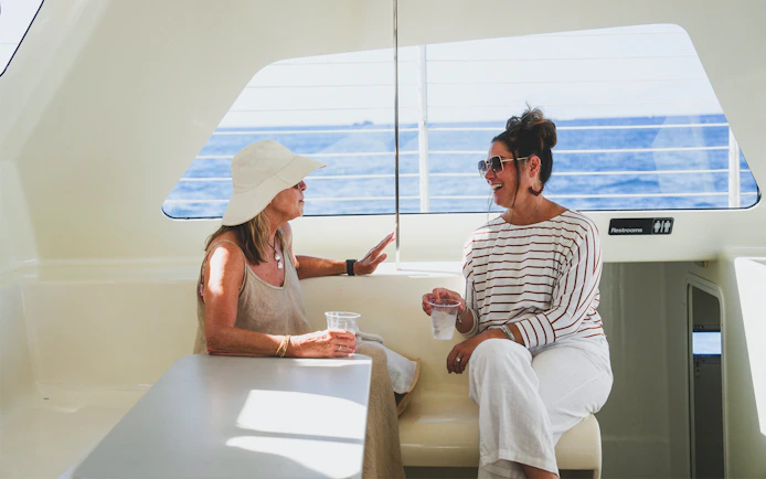 Women enjoying drinks on a Waikiki sailboat with ocean view.