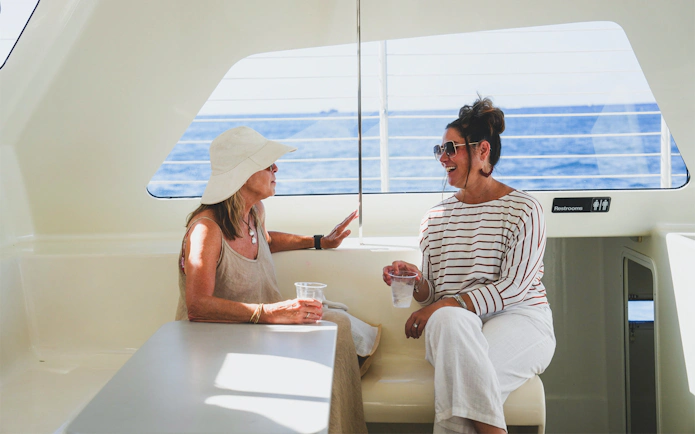 Women enjoying drinks on a Waikiki sailboat with ocean view.