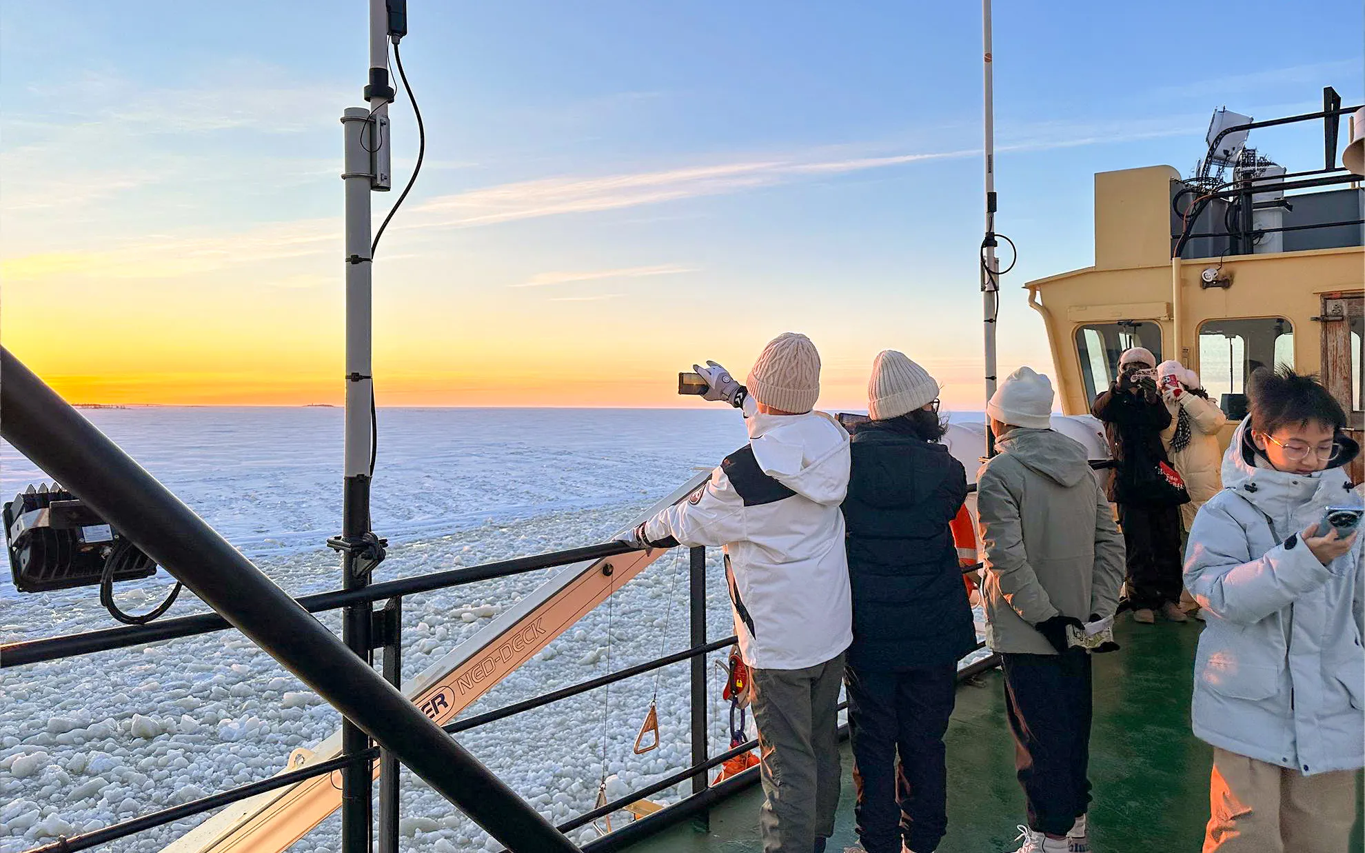 Tourists on Icebreaker Arktis cruise capturing sunset over frozen sea, Kemi.