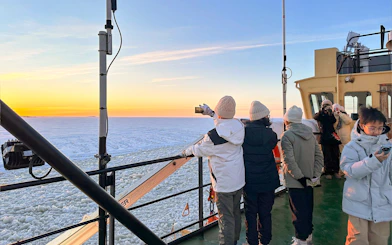 Tourists on Icebreaker Arktis cruise capturing sunset over frozen sea, Kemi.