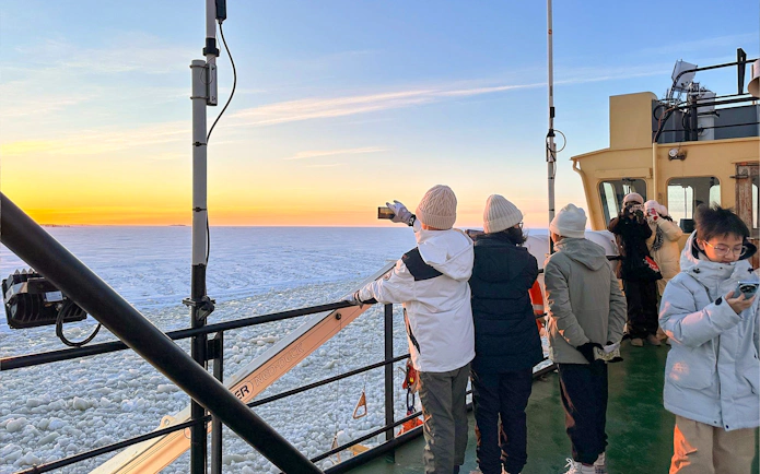 Tourists on Icebreaker Arktis cruise capturing sunset over frozen sea, Kemi.