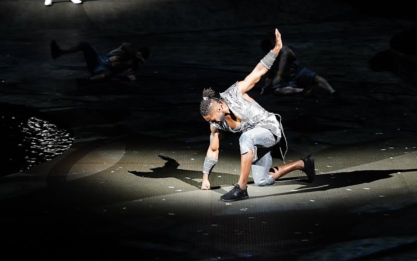 Performer on stage during La Perle show in Dubai, with dramatic lighting and acrobatic pose.