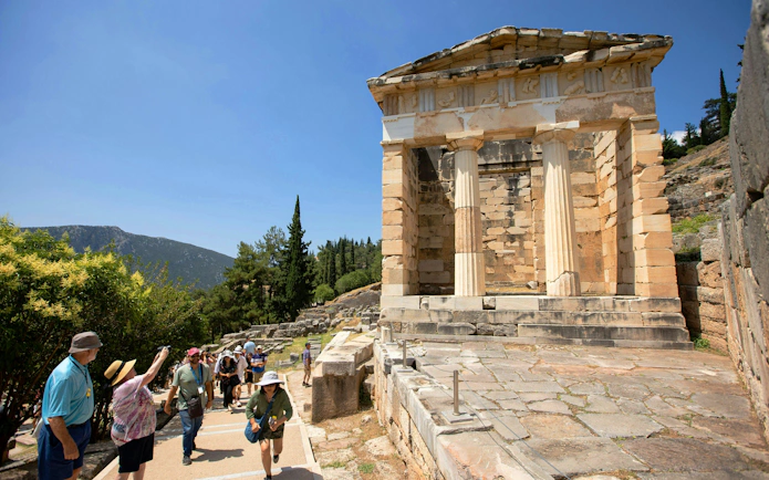 Ancient ruins of the Treasury of Athens at Delphi with tourists exploring the site.