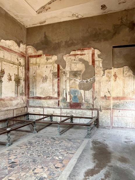 Herculaneum Ruins interior with ancient frescoes and stone benches.