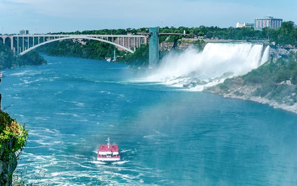 Boat approaching Niagara Falls with Rainbow Bridge in Ontario, Canada.