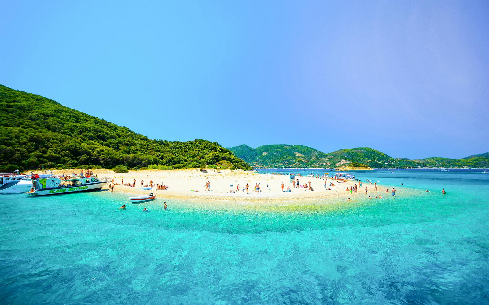 Glass-bottom boat near Zakynthos Turtle Island with tourists swimming and relaxing on the beach.