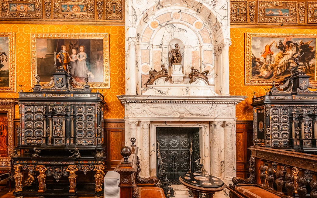 Historical royal room with ornate fireplace and paintings in Peles Castle, Romania.