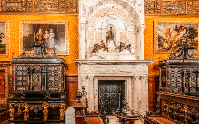 Historical royal room with ornate fireplace and paintings in Peles Castle, Romania.