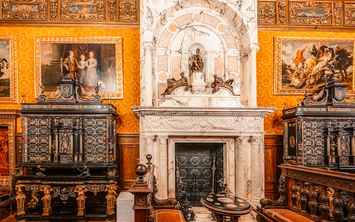 Historical royal room with ornate fireplace and paintings in Peles Castle, Romania.