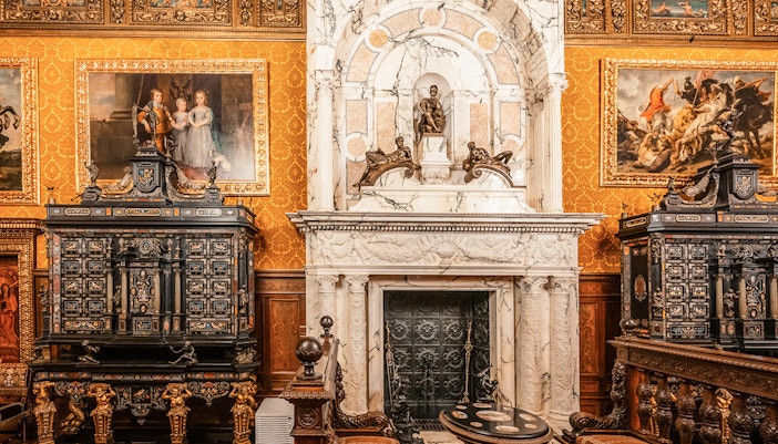 Historical royal room with ornate fireplace and paintings in Peles Castle, Romania.