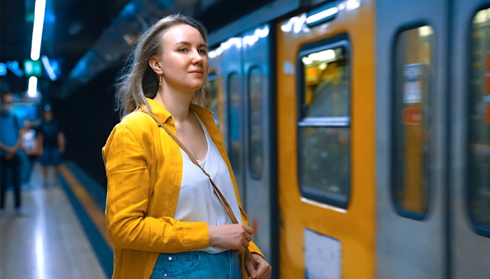 Woman standing on platform at Napoli Porta Nolana Station with train in background.