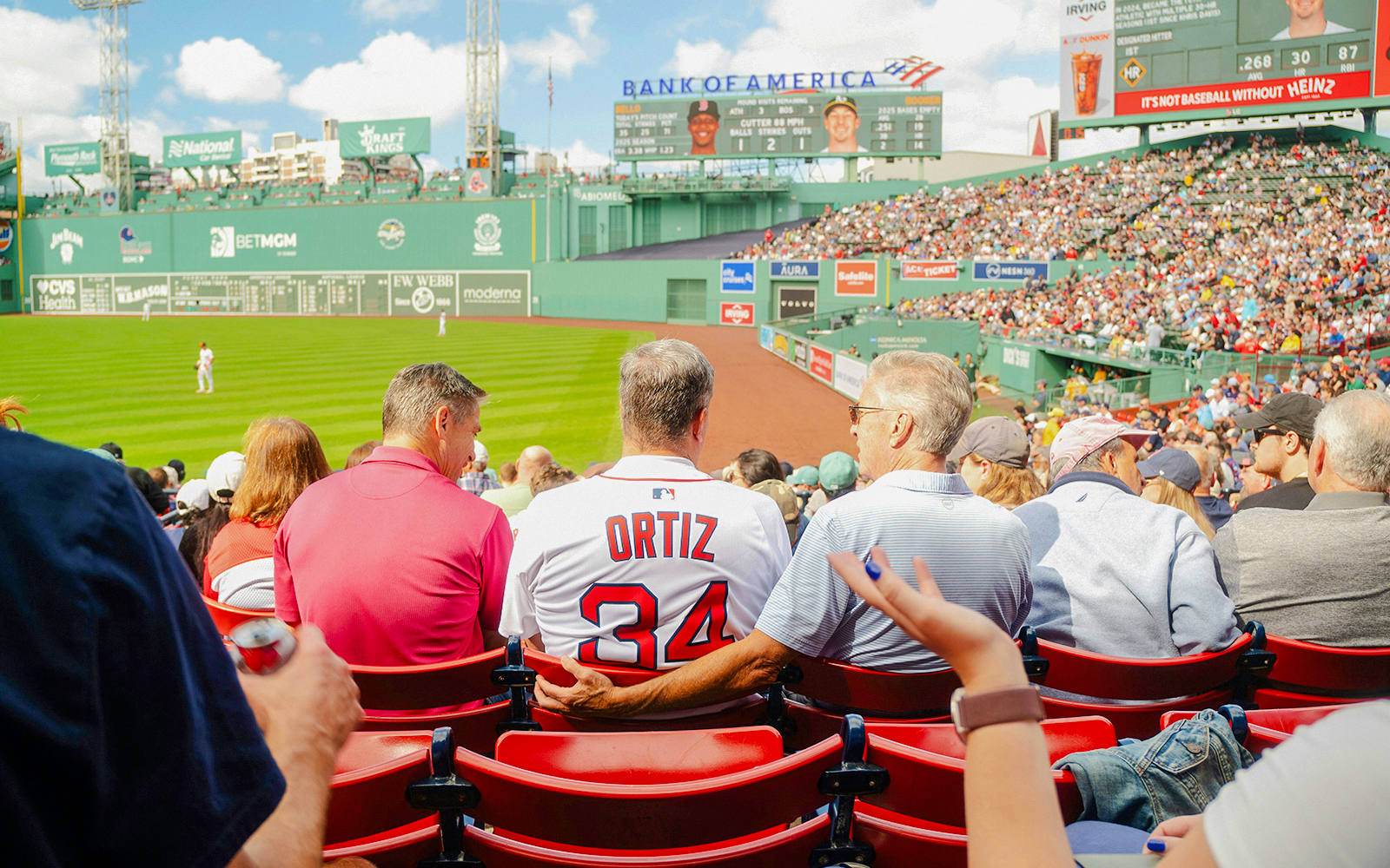 Fans watching a baseball game at Fenway Park, one wearing a Red Sox Ortiz jersey.