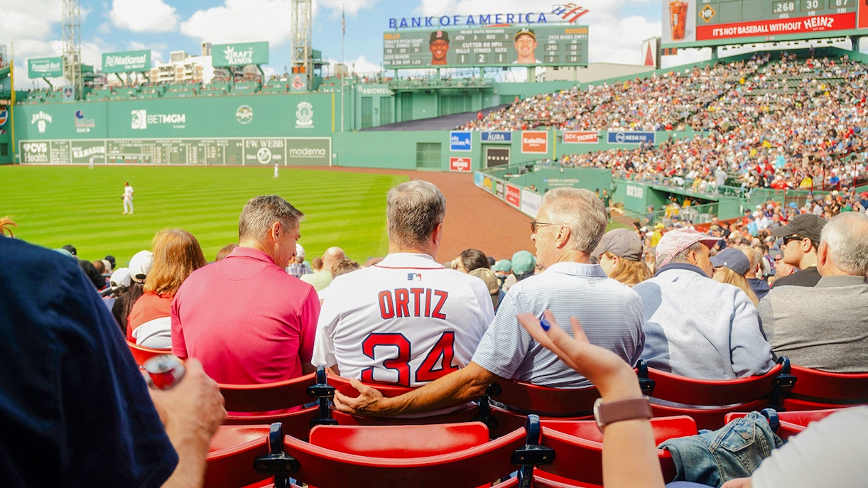 Fans watching a baseball game at Fenway Park, one wearing a Red Sox Ortiz jersey.
