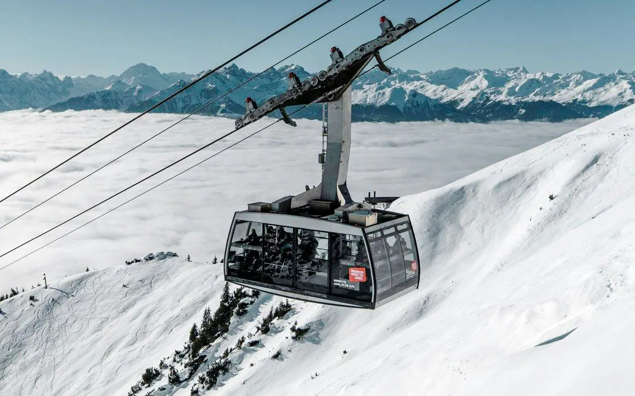 Cable car ascending snowy mountain at Innsbruck with Alps in background.