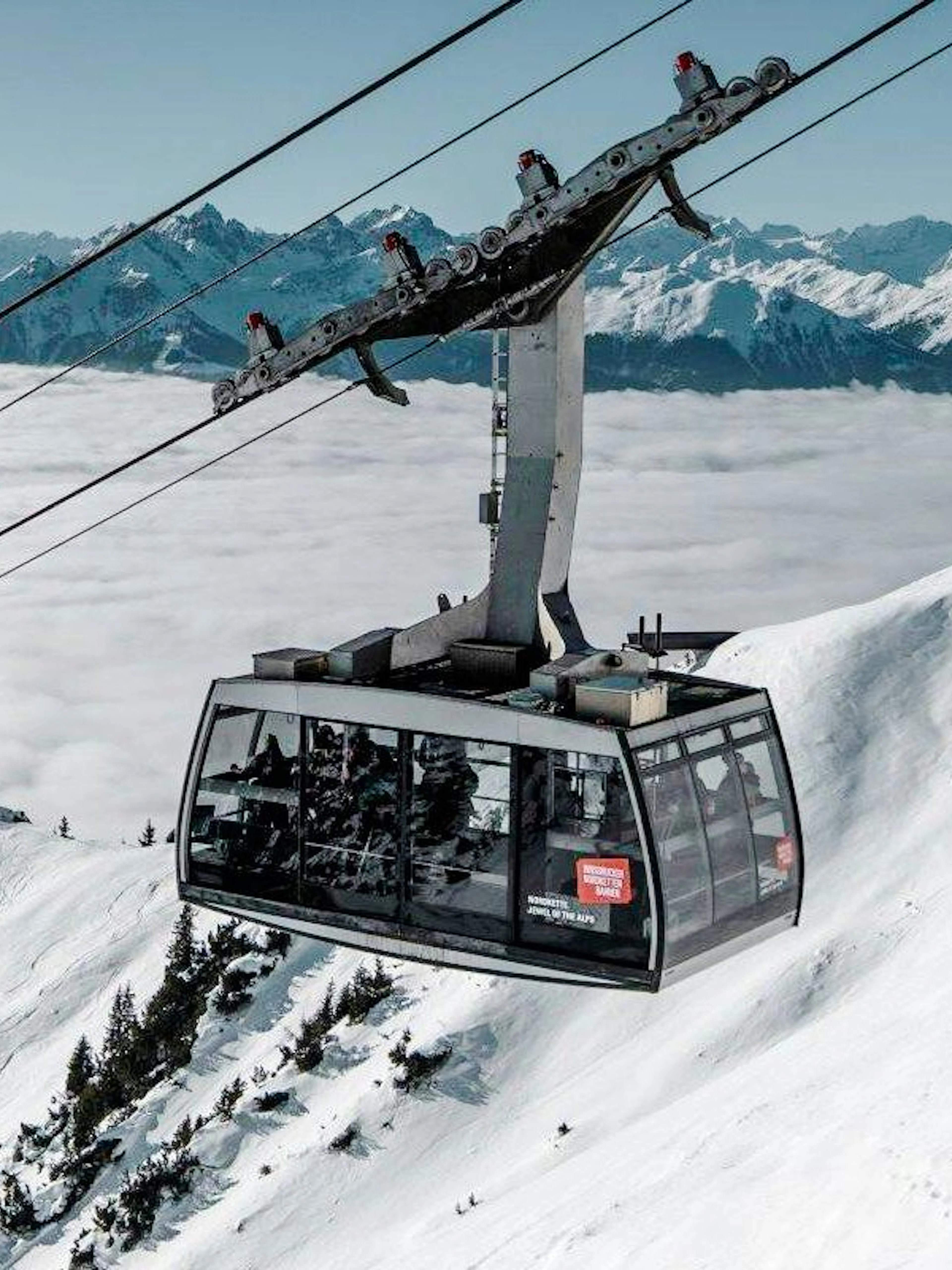 Cable car ascending snowy mountain at Innsbruck with Alps in background.