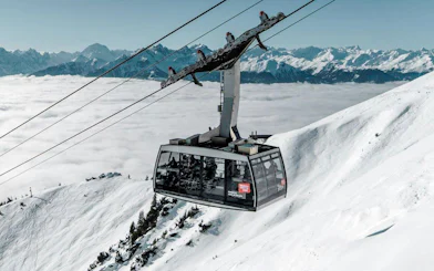 Cable car ascending snowy mountain at Innsbruck with Alps in background.