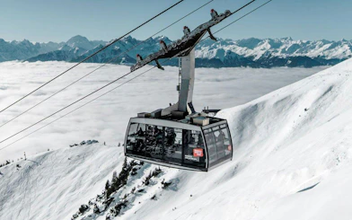 Cable car ascending snowy mountain at Innsbruck with Alps in background.