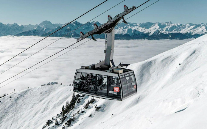 Cable car ascending snowy mountain at Innsbruck with Alps in background.