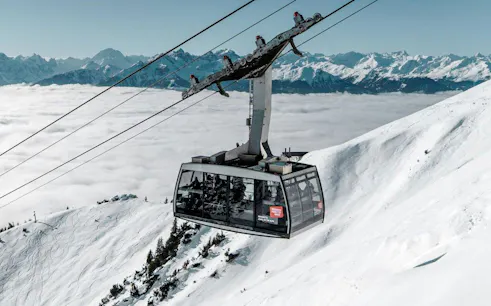 Cable car ascending snowy mountain at Innsbruck with Alps in background.