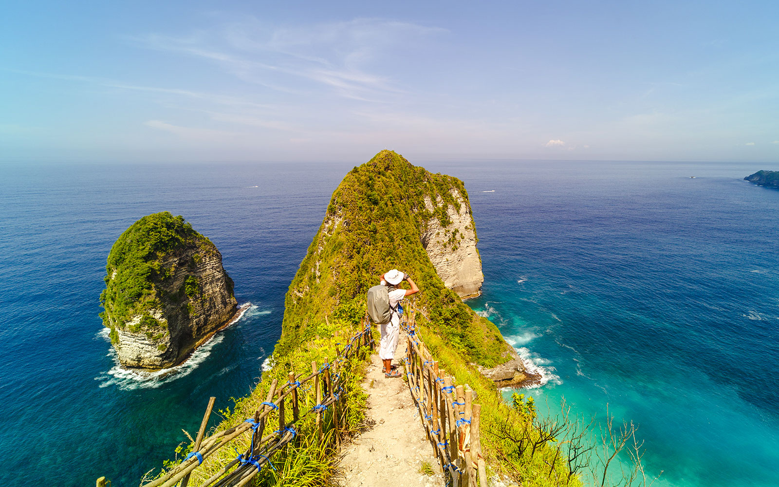Backpacker on Kelingking Beach cliff, Nusa Penida, overlooking ocean.