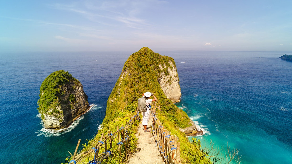 Backpacker on Kelingking Beach cliff, Nusa Penida, overlooking ocean.