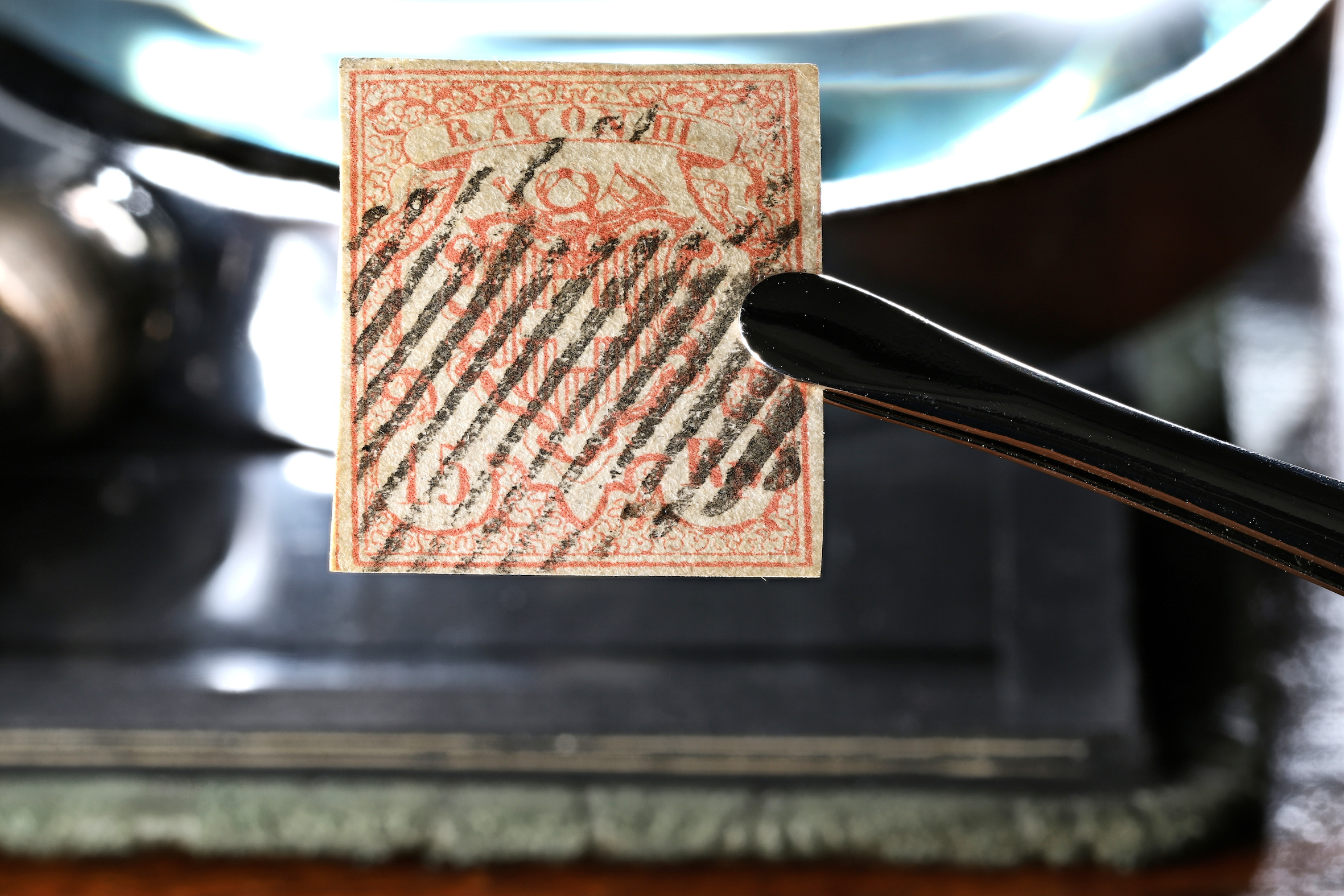 Stamp held by tweezers with magnifying glass in background.