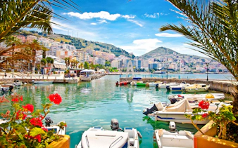 Boats docked at Saranda Harbour with cityscape and hills in the background.