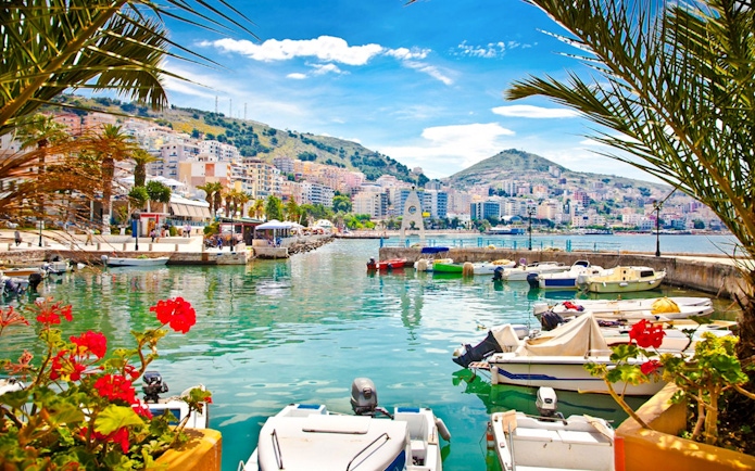 Boats docked at Saranda Harbour with cityscape and hills in the background.