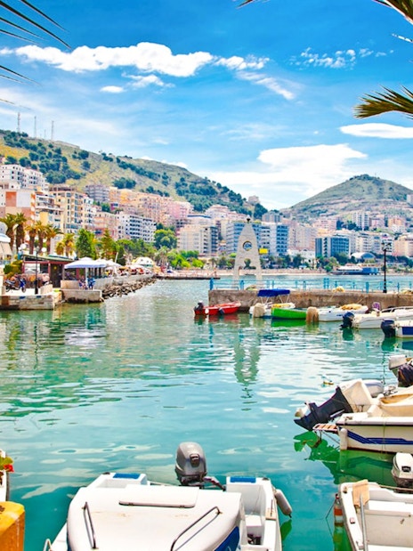 Boats docked at Saranda Harbour with cityscape and hills in the background.